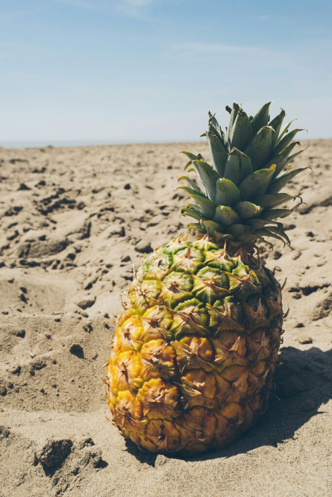 Juicy pineapple on sandy beach under bright blue sky, embodying tropical summer vibes.