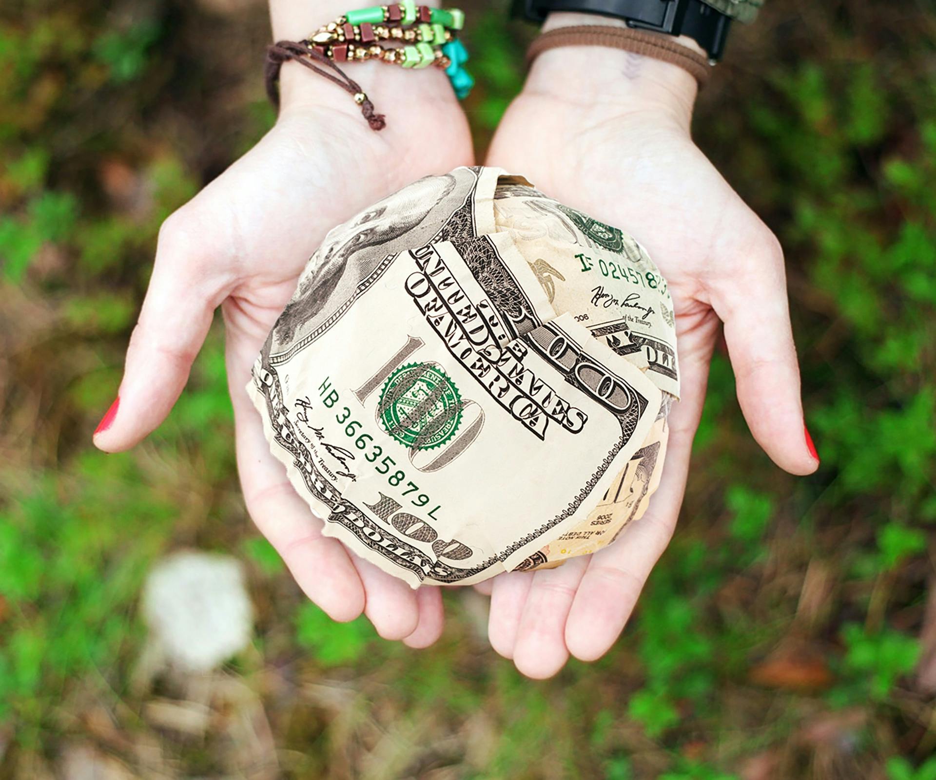 Hands holding crumpled money outdoors, symbolizing charity and financial support.