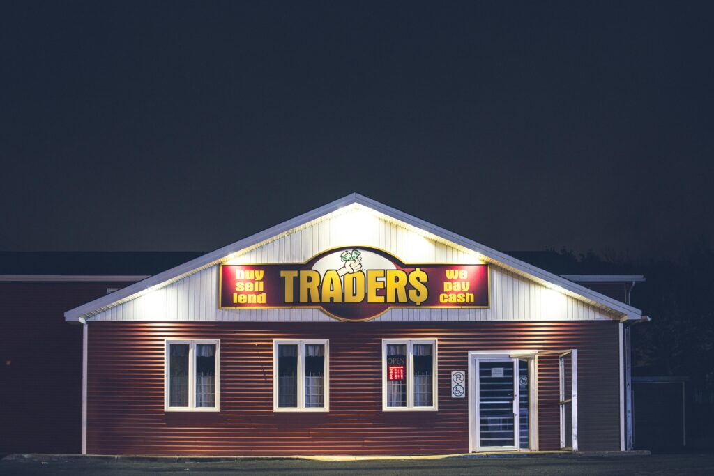 Illuminated trader's storefront at night displaying vibrant signage with business motifs.