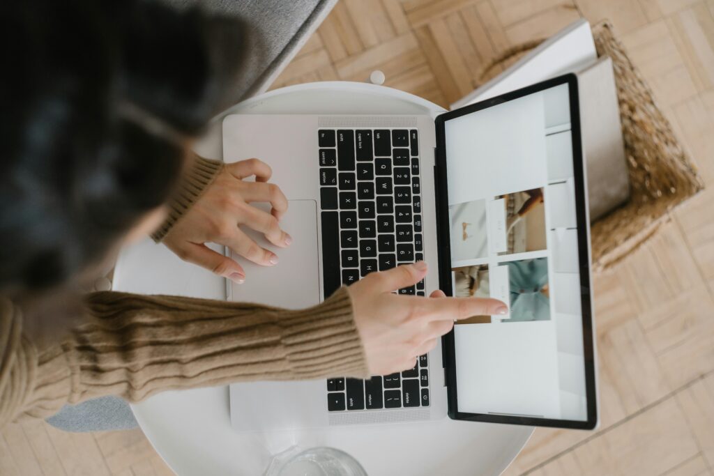 Top view of a woman pointing at laptop screen while browsing photos indoors, showcasing modern digital lifestyle.